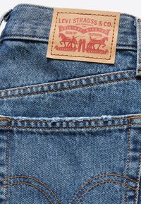 Parche de cuero de Levi Strauss & Co. en unos pantalones vaqueros de mezclilla azules, mostrando dos caballos tirando de la mezclilla hacia afuera con costuras cosidas.