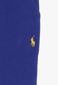 Tela de algodón azul con un pequeño logo de jugador de polo bordado en dorado en el lateral. Textura suave con un diseño ajustado.