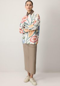 Suéter de punto con un colorido patrón floral sobre fondo blanco, combinado con una falda beige y zapatillas blancas.