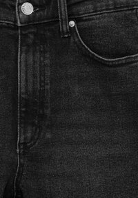 Jean en denim noir avec texture lisse, design classique à cinq poches, rivets décoratifs et légère décoloration le long des coutures.