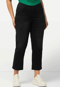 Pantalones de mezclilla negros con cintura ajustada y piernas rectas ligeramente recortadas. Combinados con una camiseta gráfica verde y zapatillas blancas.