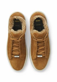 Brązowe zamszowe sneakersy z futrzanym wnętrzem, beżowe podeszwy, markowy metalowy znaczek BOSS na sznurówkach, oraz napis "BOSS" wewnątrz, wyprodukowane we Włoszech.