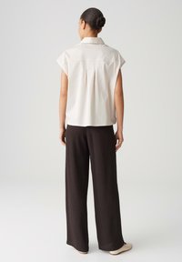 Lichtbeige shirt met kapmouwen en een geplooide rugdetail, gecombineerd met een losvallende, donkerbruine broek met wijde pijpen. Minimalistische stijl, eenvoudig ontwerp.