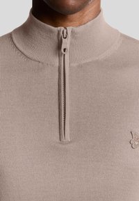 Beige Halbzip-Pullover mit geripptem Kragen, strukturiertem Stoff und einem kleinen Logo-Akzent auf der Brust. Reißverschluss in passender Farbe.