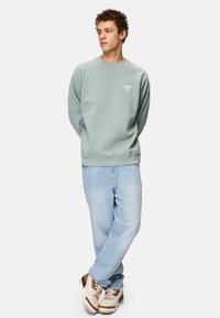 Minttivihreä collegepaita, jossa on ribbireunukset kaula-aukossa ja hihansuissa, yhdistettynä vaaleansinisiin farkkuihin ja beigeihin lenkkareihin, joissa on ruskeita yksityiskohtia.