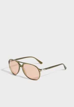 Lunettes de soleil aviateur vert olive, avec des verres rose pâle et de fines branches en métal, présentées de biais sur un fond clair.
