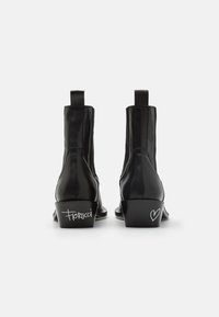 Botas de tobillo de cuero negro con un diseño elegante, tacón bajo y marca distintiva en los laterales. Textura suave con lengüetas de tiro.