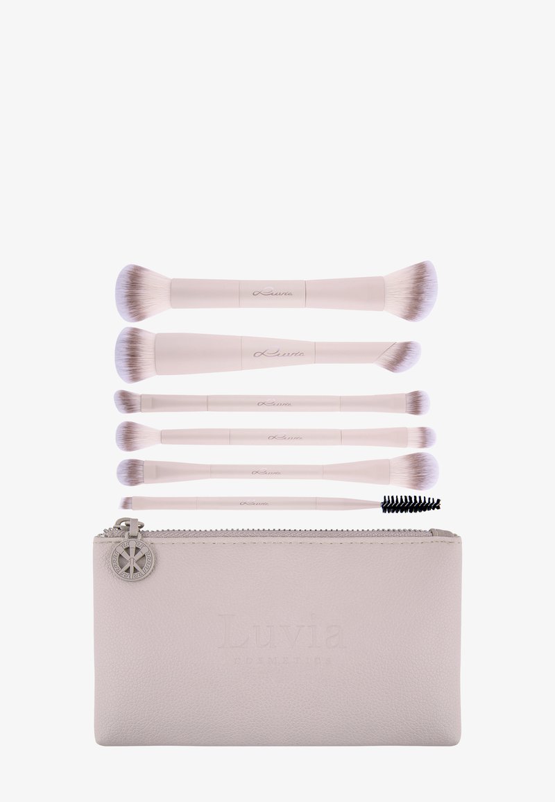 Sei pennelli da trucco rosa chiaro di varie forme e dimensioni sopra una pochette coordinata con cerniera e un ciondolo in metallo rotondo.
