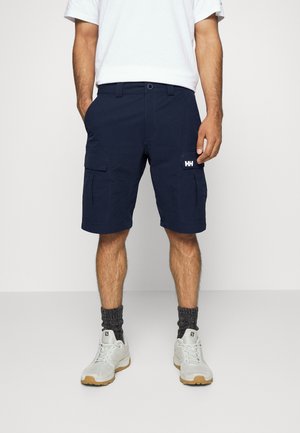 Pantaloni cargo blu navy con molte tasche laterali, realizzati in tessuto morbido, con orlo arrotolato e patch con logo sul davanti. Indossati con scarpe bianche.