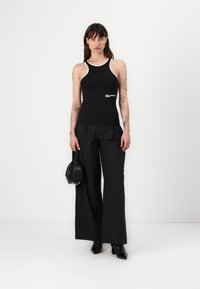 Top negro sin mangas con detalles en blanco, diseño ajustado y logo; combinado con pantalones anchos negros y zapatos de tacón negros.