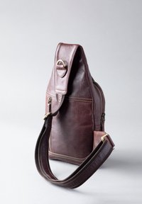 Leather shoulder bag in dark brown, featuring a textured finish, gold hardware accents, a side zipper, and a wide, woven strap.