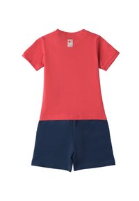 Camiseta corta roja de manga corta con un escote redondo, combinada con pantalones cortos azul marino. La tela parece suave y ligera. Etiqueta visible en la camiseta.