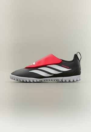 Zapato de fútbol Adidas Predator en blanco y negro con solapa roja y suela gris con tacos, mostrado de perfil sobre fondo neutro.