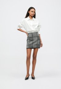 Weißes Hemd mit Knöpfen, karierten Minirock in Schwarz und Weiß, schlanker Schnitt, kombiniert mit schwarzen spitzen Ballerinas. Schlichtes Design, lässiger Stil.