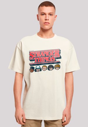 Off-white cotton t-shirt featuring a graphic print with the text "Stranger Things" and illustrated character faces. Short sleeves, crew neck.