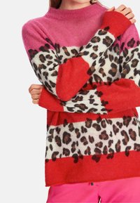 Strickpullover mit pink-rot gestreiftem Design und einem Leopardenmusterband, aus weichem, flauschigem Material. Hoher Ausschnitt und lange Ärmel.