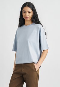 Ανοιχτό μπλε βαμβακερό t-shirt με κοντά μανίκια και χαλαρή εφαρμογή, με μικρό λογότυπο στην αριστερή πλευρά του στήθους.