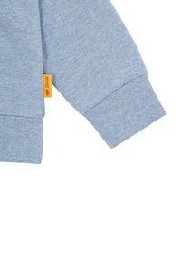 Felpa azzurra con una morbida texture, dotata di polsini ripiegati e di un piccolo etichetta gialla con il marchio cucita di lato.