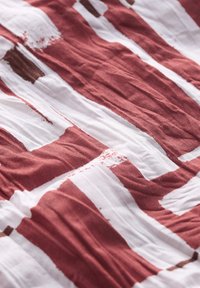 Textil que presenta un patrón de amplias y desiguales rayas color burdeos y blancas con arrugas texturizadas, diseñado en una tela ligera.