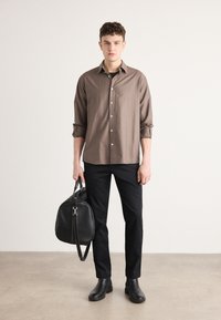 Bruin button-up shirt met opgerolde mouwen, gecombineerd met zwarte slim-fit broek en zwarte leren enkellaarsjes, houdend een zwarte leren tas.