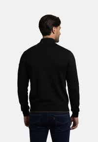 Suéter negro de punto con cuello alto, diseño ajustado y puños acanalados. Combinado con jeans azul con un sutil detalle de logo.