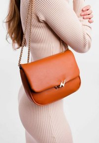 Oranžová kožená crossbody taška se zlatými kovovými doplňky a řetízkovým popruhem. Obsahuje klopu a hladký povrch.