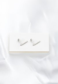 Orecchini a barre d'argento con gemme trasparenti incastonate in una linea retta, caratterizzati da un design con perno e retro, esposti su una superficie morbida e bianca.