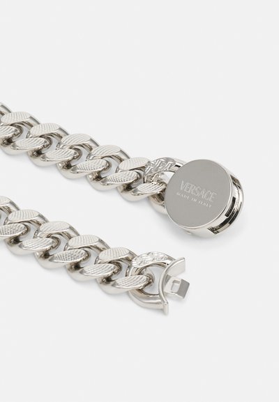 Srebrna zapestnica s teksturiranimi povezavami z listnatim vzorcem in okroglo sponko, ki je gravirana z besedilom "Versace Made in Italy."