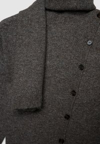 Cardigan marrone lavorato a maglia con collo alto, caratterizzato da un tessuto strutturato, sei bottoni scuri e un design accogliente con pieghe all'altezza del collo.