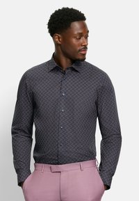 Camicia a maniche lunghe di un blu navy scuro con un motivo geometrico in blu chiaro e bordeaux. Presenta un colletto classico e chiusura con bottoni frontale.