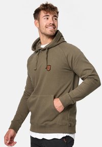 Sudadera verde oliva hecha de una suave mezcla de algodón, con un bolsillo tipo canguro en la parte frontal, capucha con cordón y un pequeño parche de logo en el pecho.