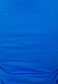 Tecido de algodão azul com uma textura suave, apresentando rugas subtis e um detalhe franzido ao longo de uma borda. O design geral é simples.