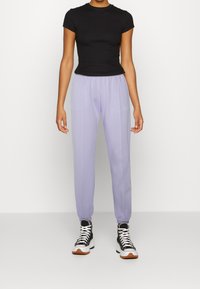 Svart kortärmad åtsittande topp, ljuslavendel sweatpants med elastiska muddar och svarta hög-top sneakers med vita sulor.