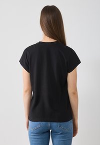 T-shirt noir à manches courtes avec un col rond, en coton, associé à un jean en denim bleu, vu de derrière.