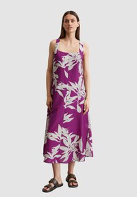 Paarse mouwloze jurk met een wit bloemenpatroon, vierkante halslijn en relaxte pasvorm, gecombineerd met bruine sandalen en een eenvoudig ontwerp.