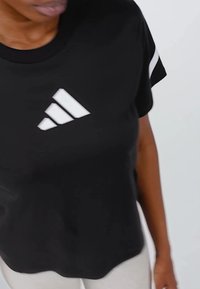 Svart t-shirt med kort ärm och rund halsringning, prydd med vit Adidas-logotyp och tre diagonala ränder. Mjukt tyg med lätt textur.