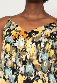 Blommönstrad klänning med V-ringning, som har en blandning av gula, orangea och blå färger, samt ribbad textur på svart tyg.