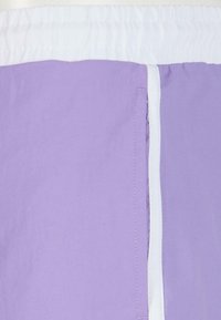 Pantaloni scurți lila cu brâu elastic alb și buzunar lateral. Textură netedă, material ușor și detalii de cusătură minime.