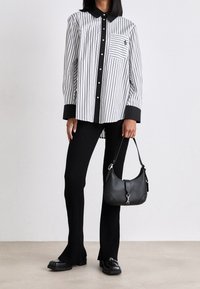 Chemise à rayures noires et blanches à boutons avec col et poignets noirs, associée à un pantalon noir côtelé et un petit sac à main noir.