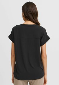 Top nera a maniche corte con scollatura rotonda, presenta un delicato dettaglio di cucitura sul retro, in tessuto morbido e con una vestibilità rilassata.