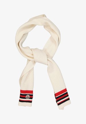 Écharpe en tricot couleur crème avec des extrémités rayées rouge, noir et blanc et un petit patch rond avec logo sur un côté.