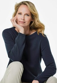 Dunkelblaues Strickpullover mit langen Ärmeln und weitem Ausschnitt, kombiniert mit hellbeigen Hosen, die eine weiche Textur und eine lockere Passform aufweisen.