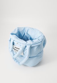 Ljusblå puffig tote-väska av mjukt material, med två böjda handtag och en rektangulär etikett med svart text.