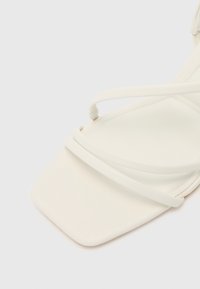 Sandale blanche à lanières avec un design à bout carré et une texture lisse, ornée de fines lanières croisées sur le dessus pour un look minimaliste.