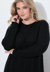 Maglione nero a maglia con motivo a treccia, maniche lunghe e scollatura rotonda. La texture appare spessa e accogliente.