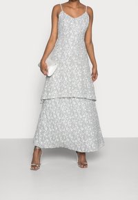 Szara maxi sukienka w kwiatowy wzór z warstwowym designem, cienkimi ramiączkami i dekoltem w kształcie litery V. Połączona z białą kopertówką i srebrnymi szpilkami.