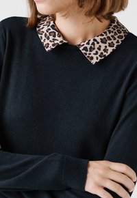 Maglione nero con tessuto strutturato, dotato di un colletto a stampa leopardata a contrasto. Il colletto ha bordi arrotondati e dettagli marroni.