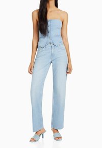 Ljusblå denimtop utan axelband med framsida knappar, tillsammans med ljusblå vida jeans. Bärs med blå klacksandaler.