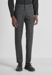 Pantalones de cuadros grises hechos de tejido textil. Diseño de pierna recta, detalle de pliegue y bolsillos laterales. Combinados con zapatos negros de cordones.