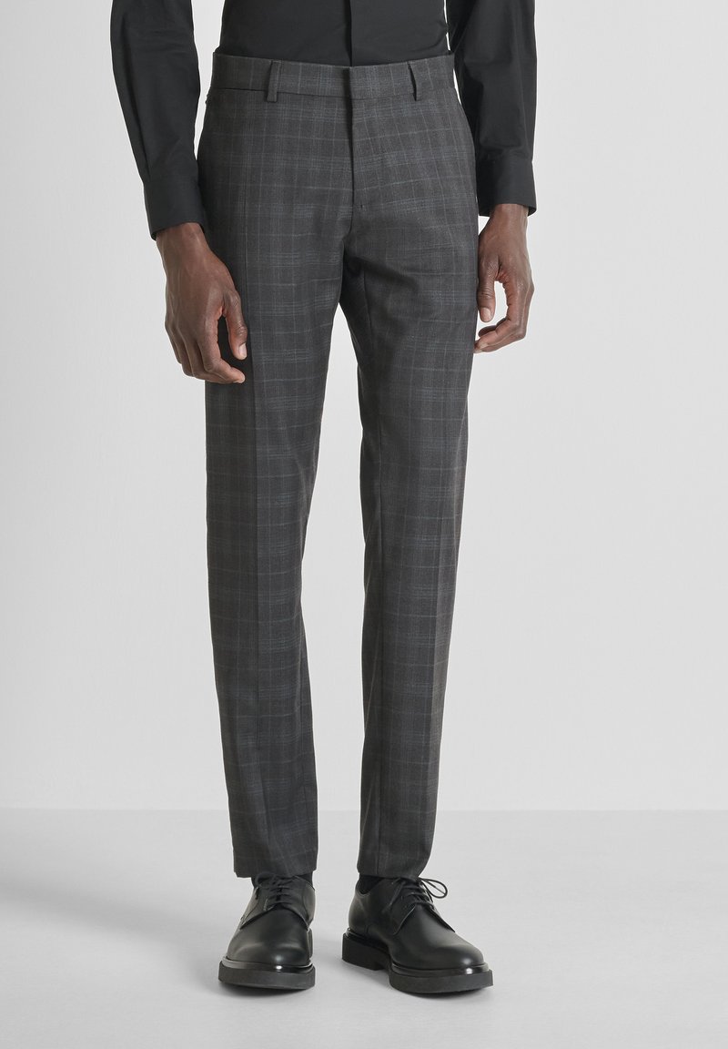 Pantalones de cuadros grises hechos de tejido textil. Diseño de pierna recta, detalle de pliegue y bolsillos laterales. Combinados con zapatos negros de cordones.